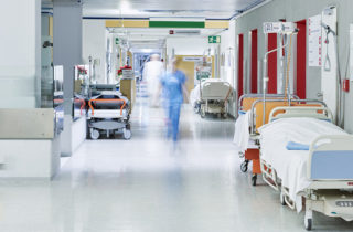 Flur im Krankenhaus mit unscharfem Arzt in Bewegung und Lift rot und Bett